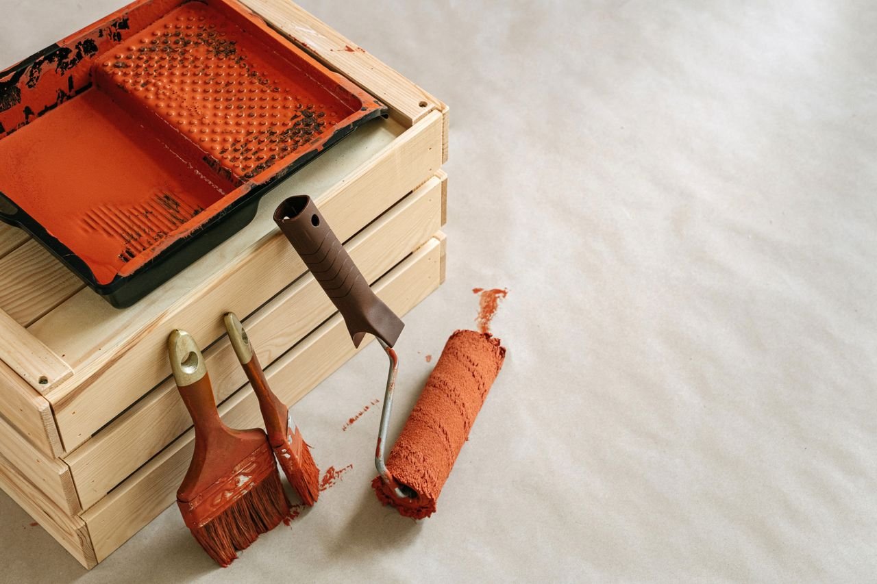 brush and paint rollers with paint spilled on floor